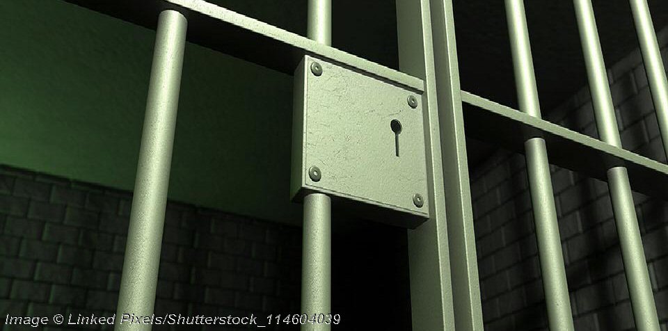 A closeup of the lock of a brick jail cell with iron bars and a door with a locking mechanism - Photo: © Copyright Linked Pixels/Shutterstock