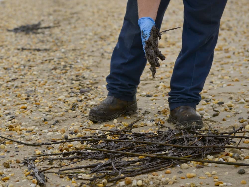 A member of a contracted oil spill response organization cleans oily debris from Slaughter Beach in Delaware as part of the Broadkill 2020 oil spill response. The Coast Guard and the Delaware Department of Natural Resources and Environmental Control are working together to identify areas where tar balls and oily debris are making landfall to facilitate an effective clean up.(U.S. Coast Guard photo by Petty Officer 3rd Class Isaac Cross.)