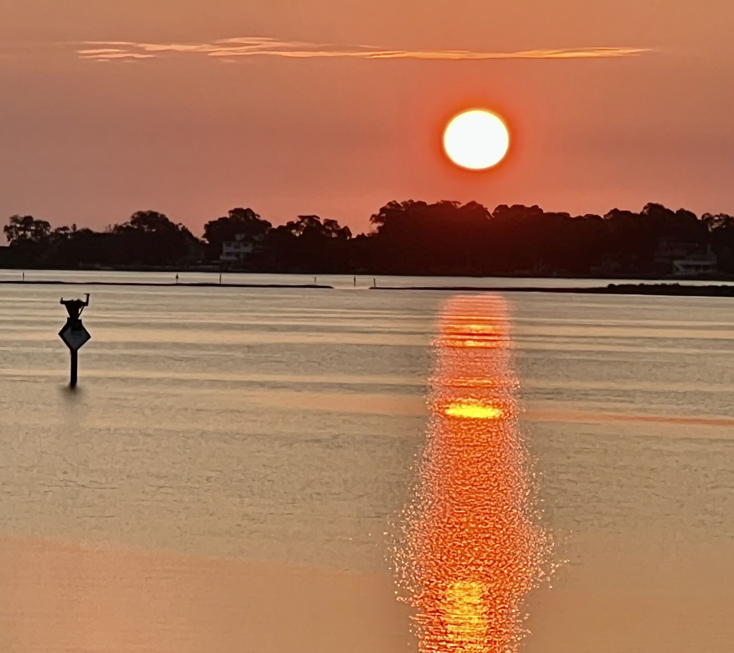 The sun rises over Indian River Bay, its reflection streaking across calm water.