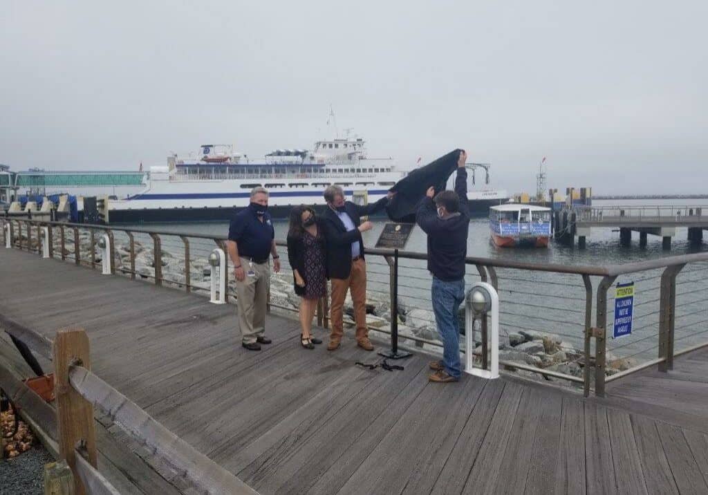 Bill Lowe Pier #1: Heath Gehrke, Director of Ferry Operations, (far right) joins with former DRBA Commissioner Bill Lowe (left) to lift the covering to unveil the bronze plaque historic marker at the entrance of Bill Lowe Pier as DRBA Executive Director Tom Cook and Bill’s wife, Rebecca, observe the proceedings.