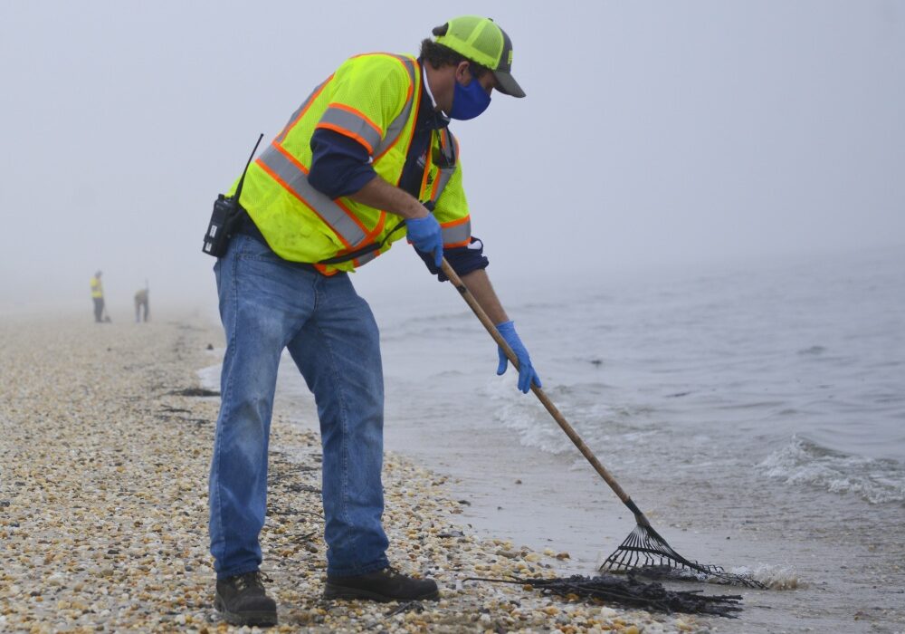 A member of a contracted oil spill response organization cleans oily debris from Slaughter Beach in Delaware as part of the Broadkill 2020 oil spill response. The Coast Guard and the Delaware Department of Natural Resources and Environmental Control are working together to identify areas where tar balls and oily debris are making landfall to facilitate an effective clean up.(U.S. Coast Guard photo by Petty Officer 3rd Class Isaac Cross.)